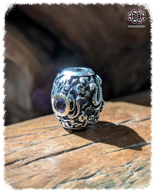 CHANG ERAWAN BarrelCharm, TWOTONE 925 STERLINGSILBER mit 18K GELBGOLD Fassung, violetter AMETHYST, stehende Frontansicht auf TEAKWOOD HOLZ, dreiköpfiges Elefantenmotiv seitlich erkennbar