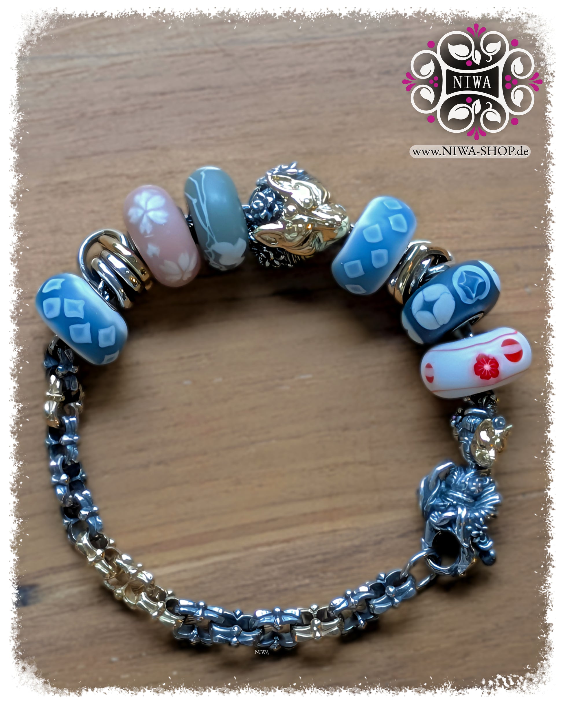 KITSUNE URAOMOTE Charm and KITSUNE URAOMOTE Lock as a set on HALF-HALF BRACELET HOPE in TwoTone 925 STERLING SILVER with 14K yellow gold, combined with TROLLBEADS KIMONO SET glass beads and two HEART spacers in TwoTone, charm as yellow gold KITSUNE MASK at the top center, lock as a GEISHA figure on the right of the bracelet, photographed on a wooden background.