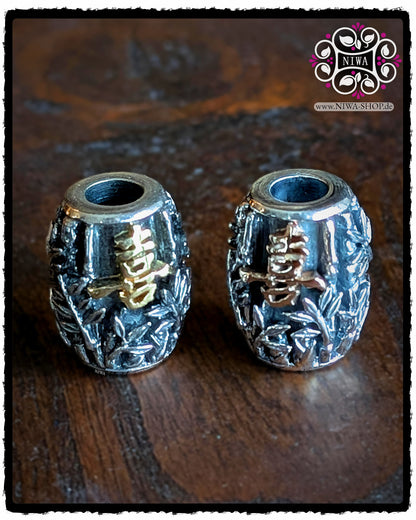 CHINESE JOY BarrelCharms aus 925 SterlingSilber mit 18K GelbGold und 18K RoséGold Schriftzeichen, beide frontal auf dunklem Holzhintergrund, feines BAMBUS-Relief und das chinesische Symbol für JOY klar erkennbar.