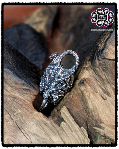 CHINESE PEACE Lock made of 925 sterling silver from MAMA MALA by NIWA, rear view without gold characters, completely covered by finely modeled chrysanthemum flowers on a wooden background.