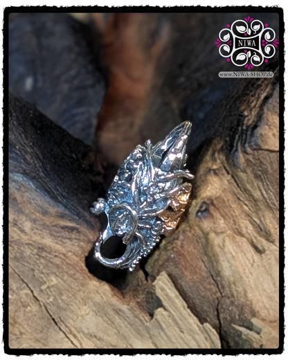 Side view of the CHINESE PEACE Lock from MAMA MALA by NIWA, detailed chrysanthemum relief with 18K rose gold characters visible on the side and an implied locking bracket, lying in a recess in the wooden background.