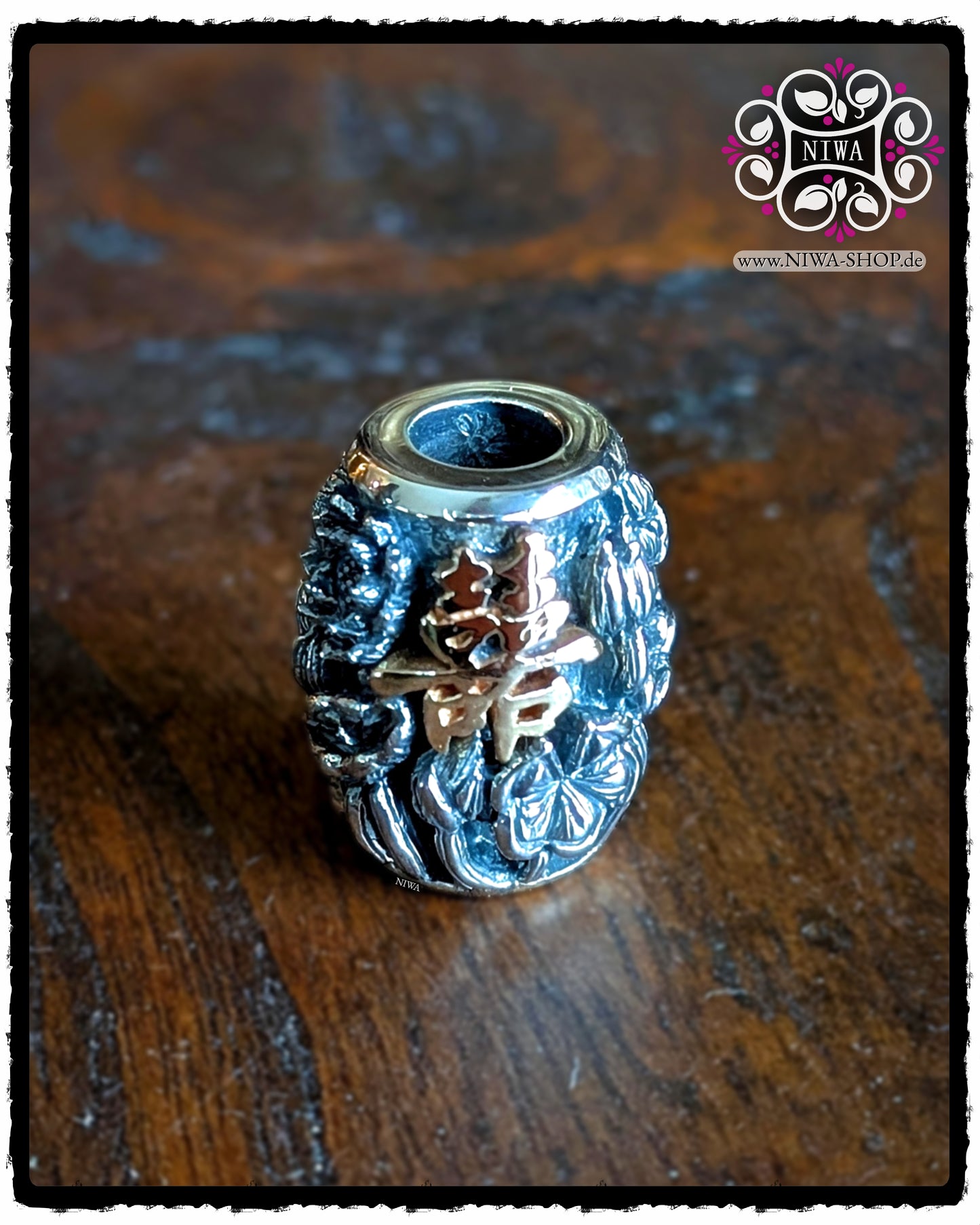 CHINESE DOUBLE HAPPINESS BarrelCharm aus 925 STERLINGSILBER mit 18K ROSÉGOLD Schriftzeichen und LOTUSBLÜTEN-Relief, frontal auf dunkler Holzoberfläche vor NIWA Logo.