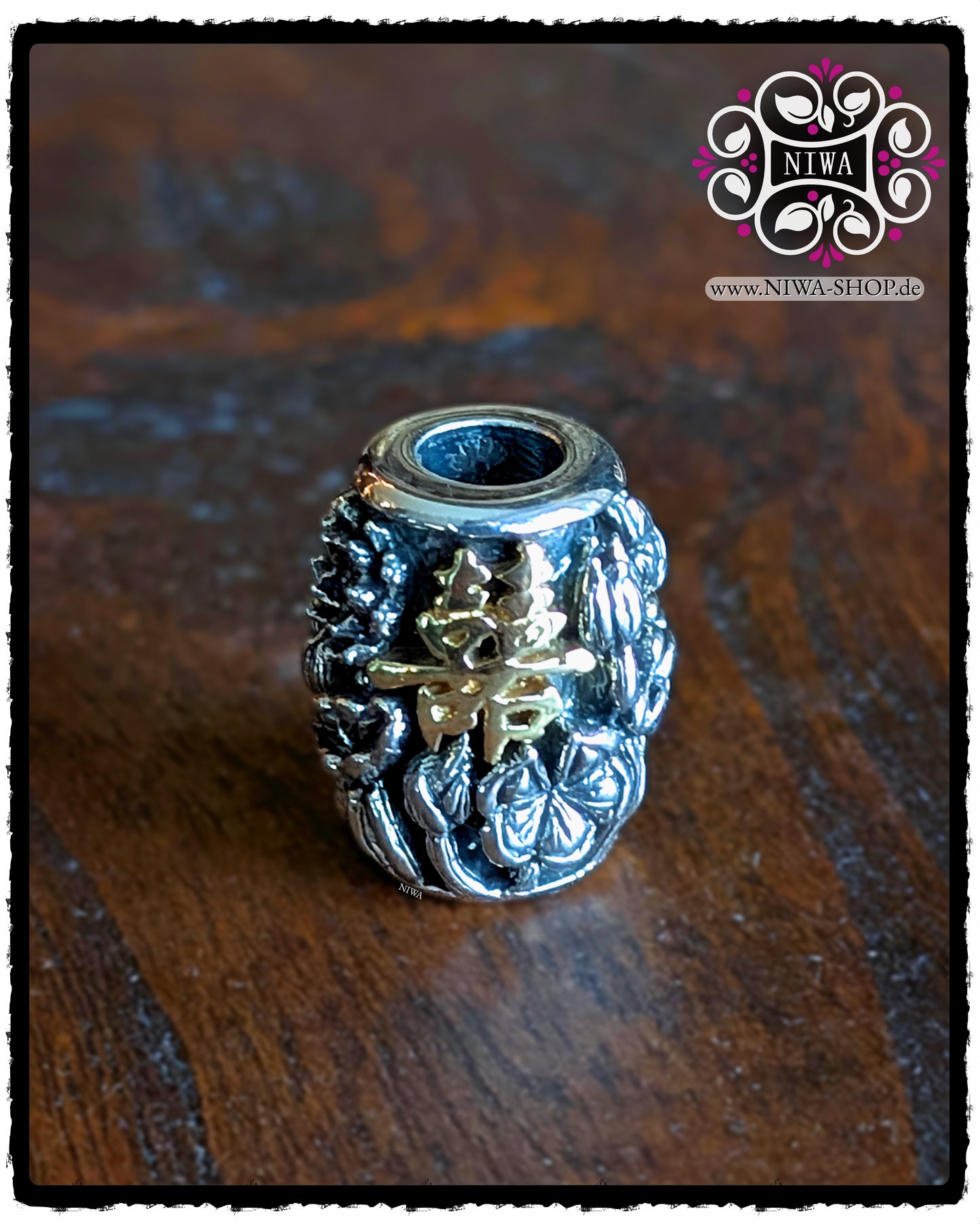 CHINESE DOUBLE HAPPINESS BarrelCharm aus 925 STERLINGSILBER mit 18K GELBGOLD Schriftzeichen und LOTUSBLÜTEN-Relief, frontal auf dunkler Holzoberfläche vor NIWA Logo.