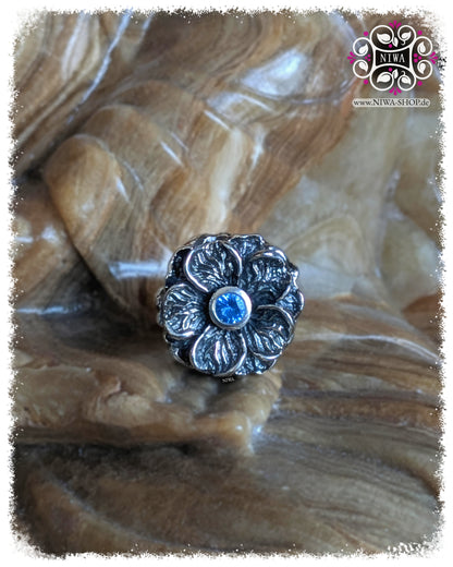FORGET ME NOT Charm, 925 Sterling Silver, Blue Quartz. Frontal view of the large forget-me-not flower with faceted blue quartz, detailed leaf structure and oxidized depressions, on a stone background.