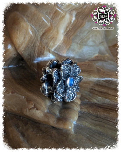 FORGET ME NOT Charm, 925 Sterling Silver, Blue Quartz. Oblique view of the flower with visible depth of the petals and central blue quartz, striking, oxidized details, on a stone background.