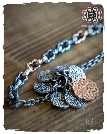 INFINITY COINS DangleSpacer in TwoTone Roségold von NIWABeads mit sieben beweglichen Coin Elementen und Half half Armband MARS im Hintergrund, seitlich auf Holz fotografiert.