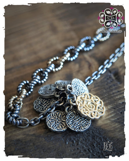 INFINITY COINS DangleSpacer in TwoTone Gelbgold von NIWABeads mit sieben beweglichen Coin Elementen und Half Half Armband FEBURA in TwoTone Gelbgold im Hintergrund, seitlich auf Holz fotografiert.