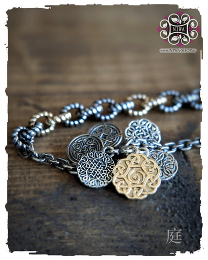 INFINITY COINS DangleSpacer von NIWABeads in TwoTone Gelbgold mit ornamentalen Silbercoins, großem Mittelcoin in 14K Gelbgold und Half Half Armband FEBURA in TwoTone Gelbgold im Hintergrund.